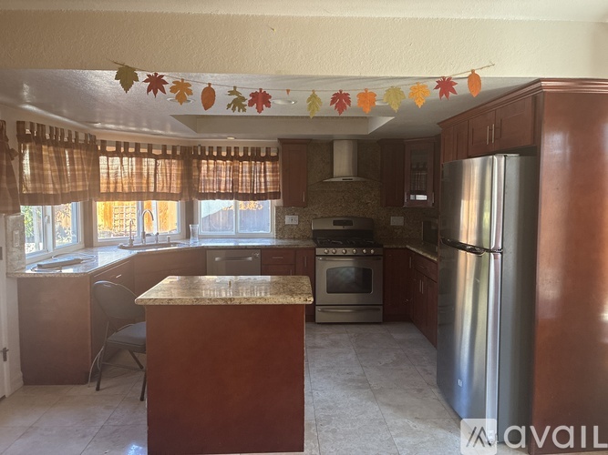 A kitchen with a refrigerator, oven, and a table with a chair.