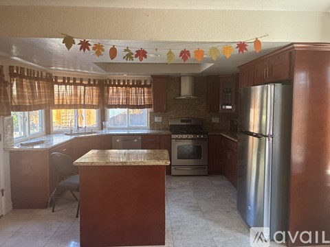 A kitchen with a refrigerator, oven, and a table with a chair.