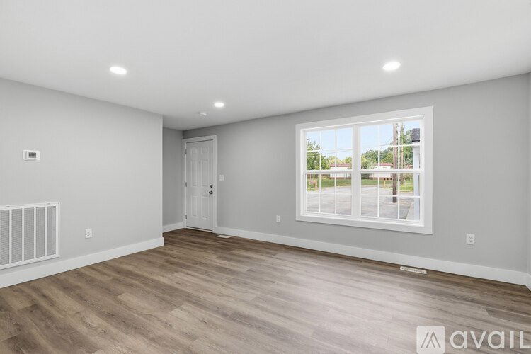 A spacious room with a large window and wooden flooring.