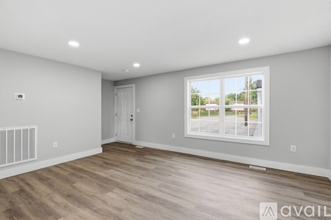 A spacious room with a large window and wooden flooring.