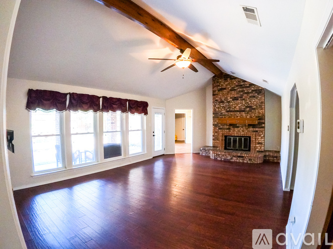 A spacious living room with wood flooring and a stone fireplace.