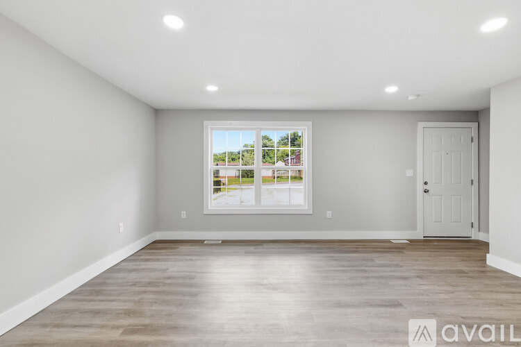 A spacious room with a large window and wooden flooring.