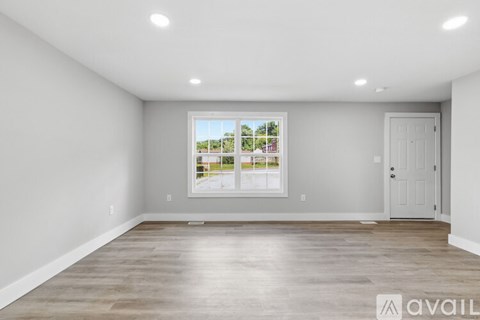 A spacious room with a large window and wooden flooring.