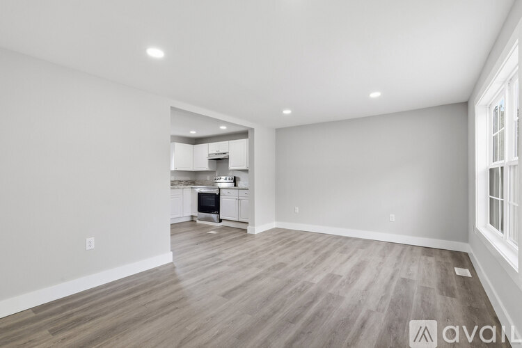 A spacious room with wooden flooring and a kitchen in the background.