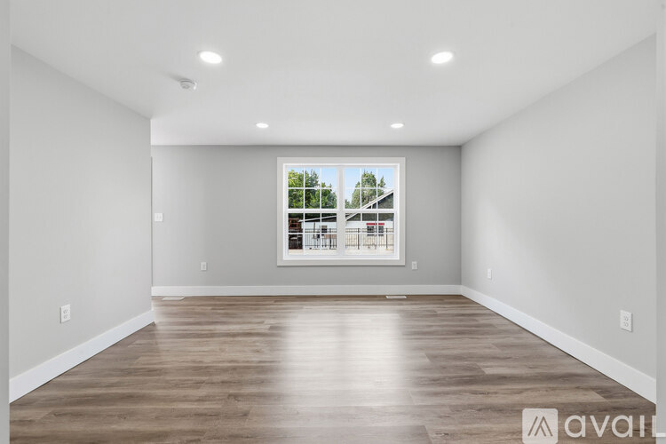 A spacious room with wooden flooring and a large window.