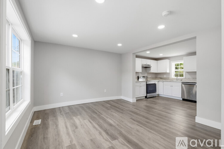 A spacious kitchen and living room with wooden flooring and white walls.