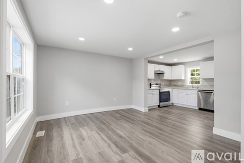A spacious kitchen and living room with wooden flooring and white walls.