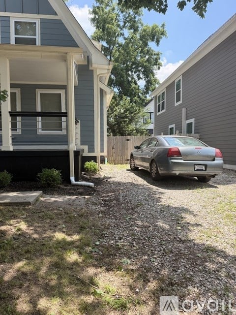 A silver car is parked in front of a grey house.