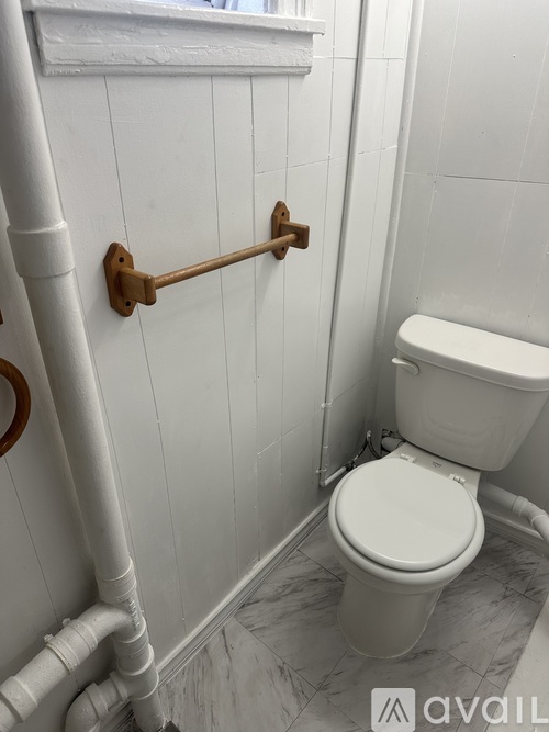 A white toilet in a bathroom with a white wall and a white pipe.