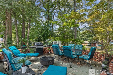 A patio with blue chairs and a fire pit surrounded by trees.