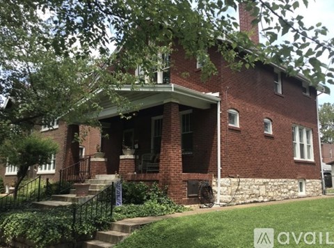 A red brick house with a porch and a tree in front.