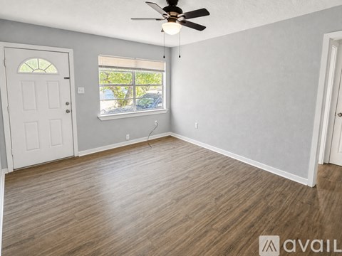 A room with a ceiling fan and a window with a view of trees and cars outside.