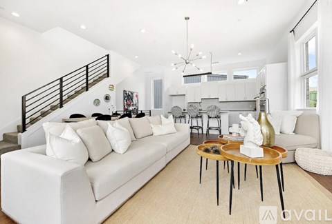 A modern living room with a staircase and a dining area in the background.