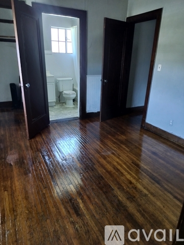 A room with wooden floors and a bathroom visible through a glass door.