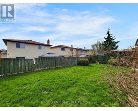 A grassy yard with a fence and houses in the background.