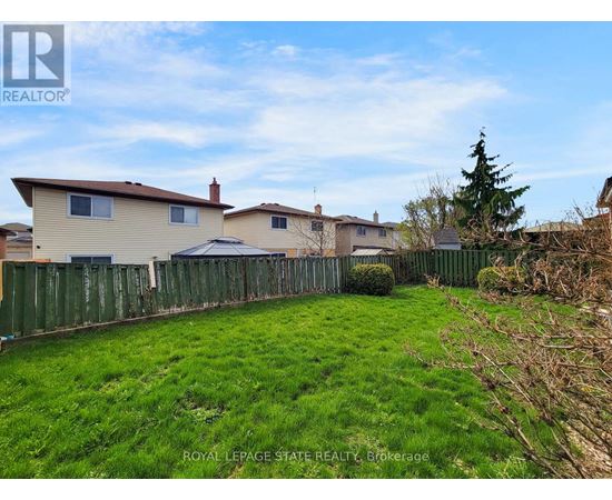 A grassy yard with a fence and houses in the background.