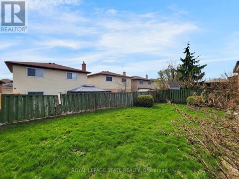 A grassy yard with a fence and houses in the background.