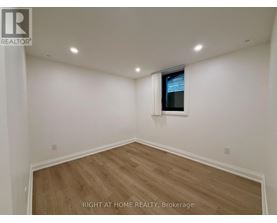 A room with wooden flooring and white walls, with a window on the wall.
