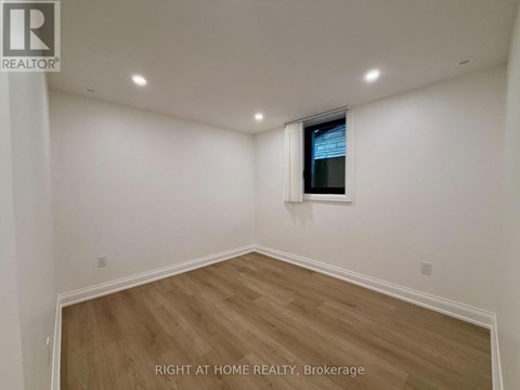 A room with wooden flooring and white walls, with a window on the wall.