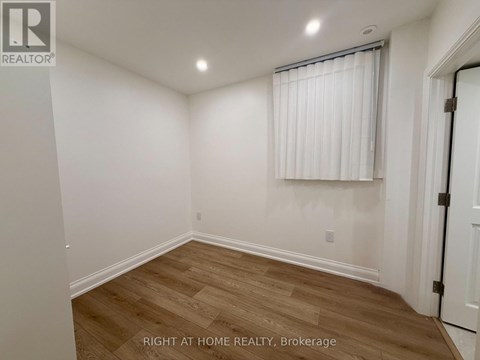 A room with white walls and wooden flooring, with a window covered by white blinds.