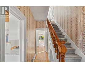 A hallway with a staircase and a doorway leading to a bedroom.
