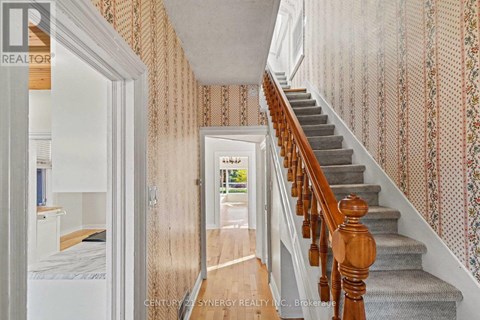 A hallway with a staircase and a doorway leading to a bedroom.