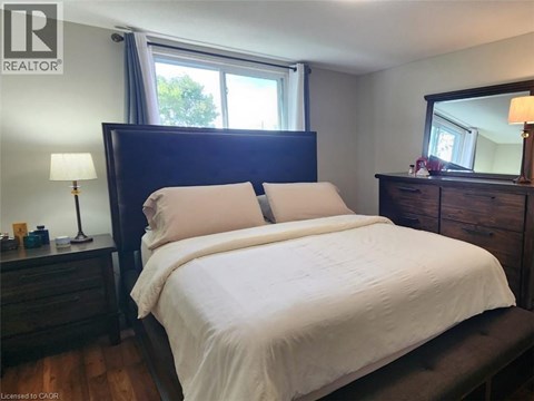 A bedroom with a large bed, a nightstand with a lamp, and a window with a view of trees.