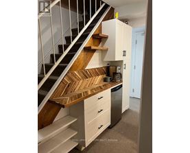 A staircase with a wooden handrail and white steps leads to a kitchen area with white cabinets and a stainless steel dishwasher.