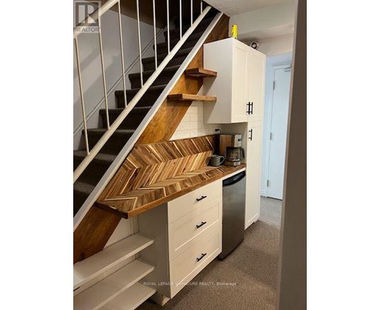 A staircase with a wooden handrail and white steps leads to a kitchen area with white cabinets and a stainless steel dishwasher.