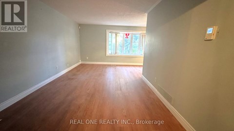 A room with wooden flooring and a window with a view of greenery outside.