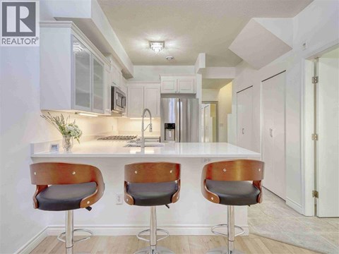 A modern kitchen with white cabinets and a bar area with two stools.