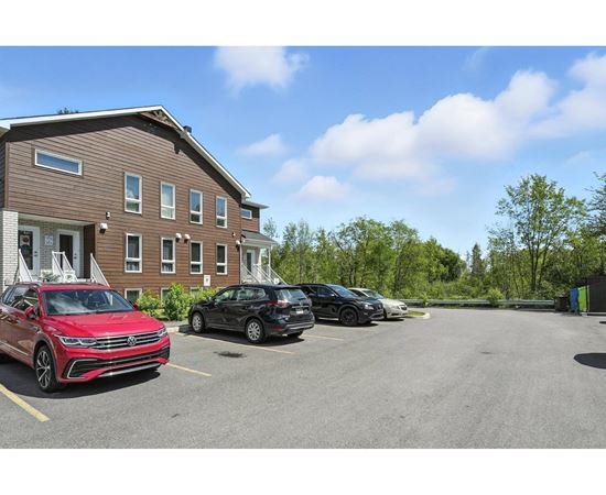 A red car is parked in a parking lot in front of a brown building.