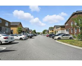 A row of cars parked on a street in front of apartment buildings.