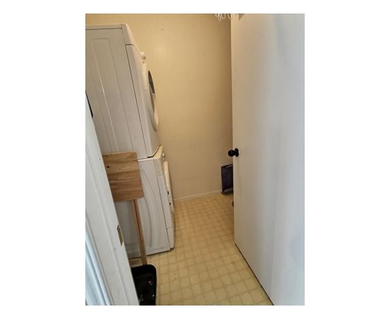 A white refrigerator is in a kitchen with a black trash can.