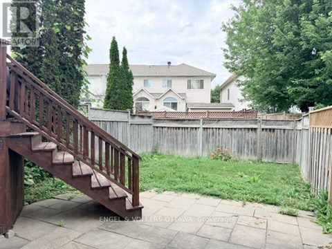 A wooden staircase leads to a house with a white fence and green trees in the background.