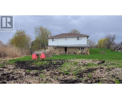 A house with a brown roof and a white exterior is surrounded by a grassy area and a dirt mound.