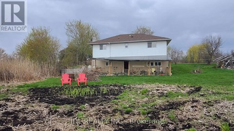 A house with a brown roof and a white exterior is surrounded by a grassy area and a dirt mound.