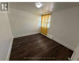 A room with wooden flooring and a window with yellow curtains.