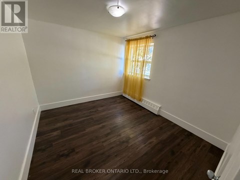 A room with wooden flooring and a window with yellow curtains.