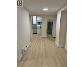 A spacious room with wooden flooring and a kitchen area in the background.