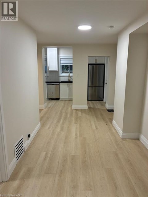 A spacious room with wooden flooring and a kitchen area in the background.