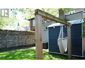 A wooden pergola with a hanging planter is in the foreground of a backyard.