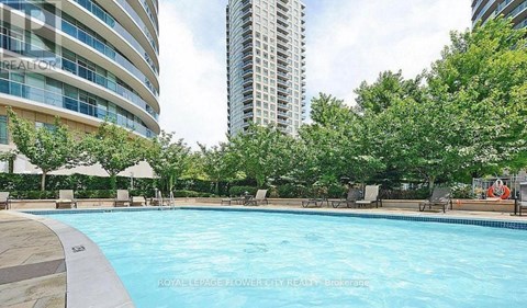 A pool surrounded by trees and chairs with a building in the background.