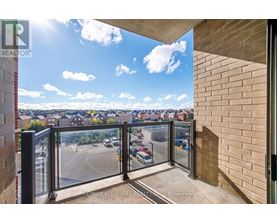 A balcony with a glass railing overlooking a parking lot and buildings.