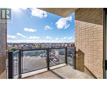 A balcony with a glass railing overlooking a parking lot and buildings.