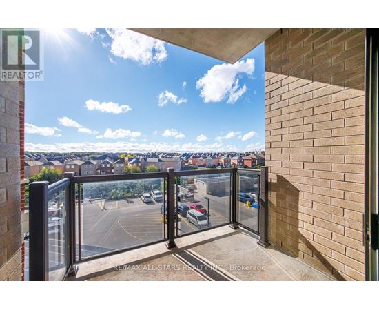 A balcony with a glass railing overlooking a parking lot and buildings.