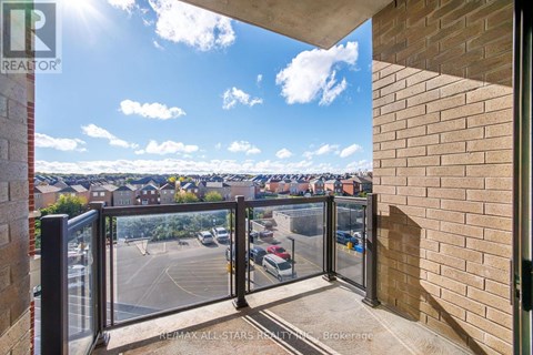 A balcony with a glass railing overlooking a parking lot and buildings.