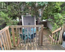 A wooden deck with a table and chairs is surrounded by greenery.