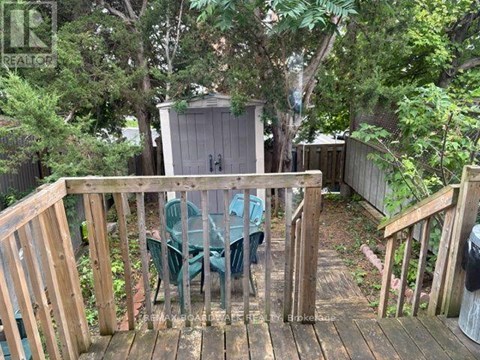 A wooden deck with a table and chairs is surrounded by greenery.
