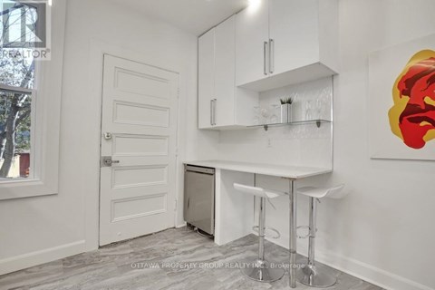 A white kitchen with a bar stool and a painting on the wall.